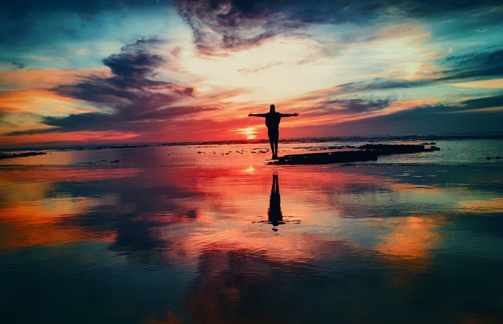 Person standing on beach with colourful sky