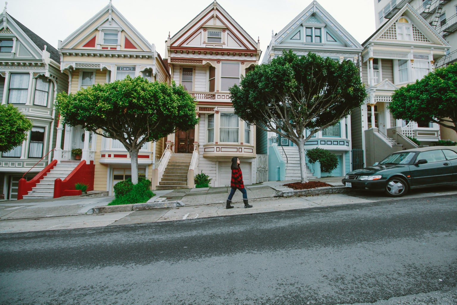 Woman walks in front of the \"Painted Lady\" buildings in San Francisco, CA.