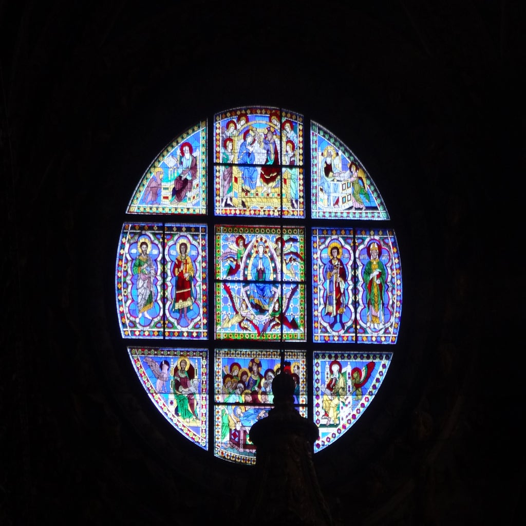 A circular stained glass window shows vibrant scenes with religious figures, divided into smaller panels.