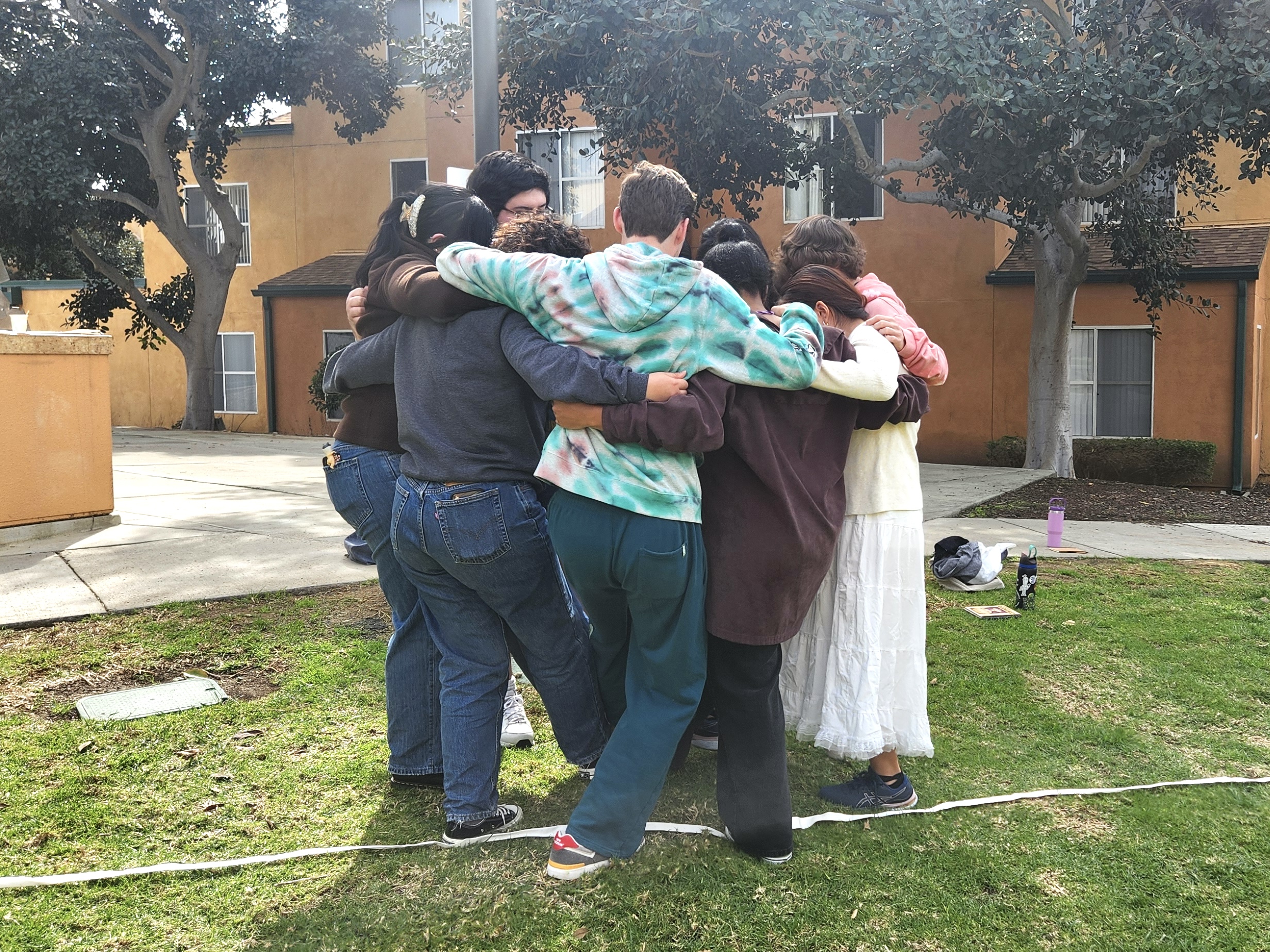 A group of people huddled together in a tight embrace outdoors during a team-building bonding activity.