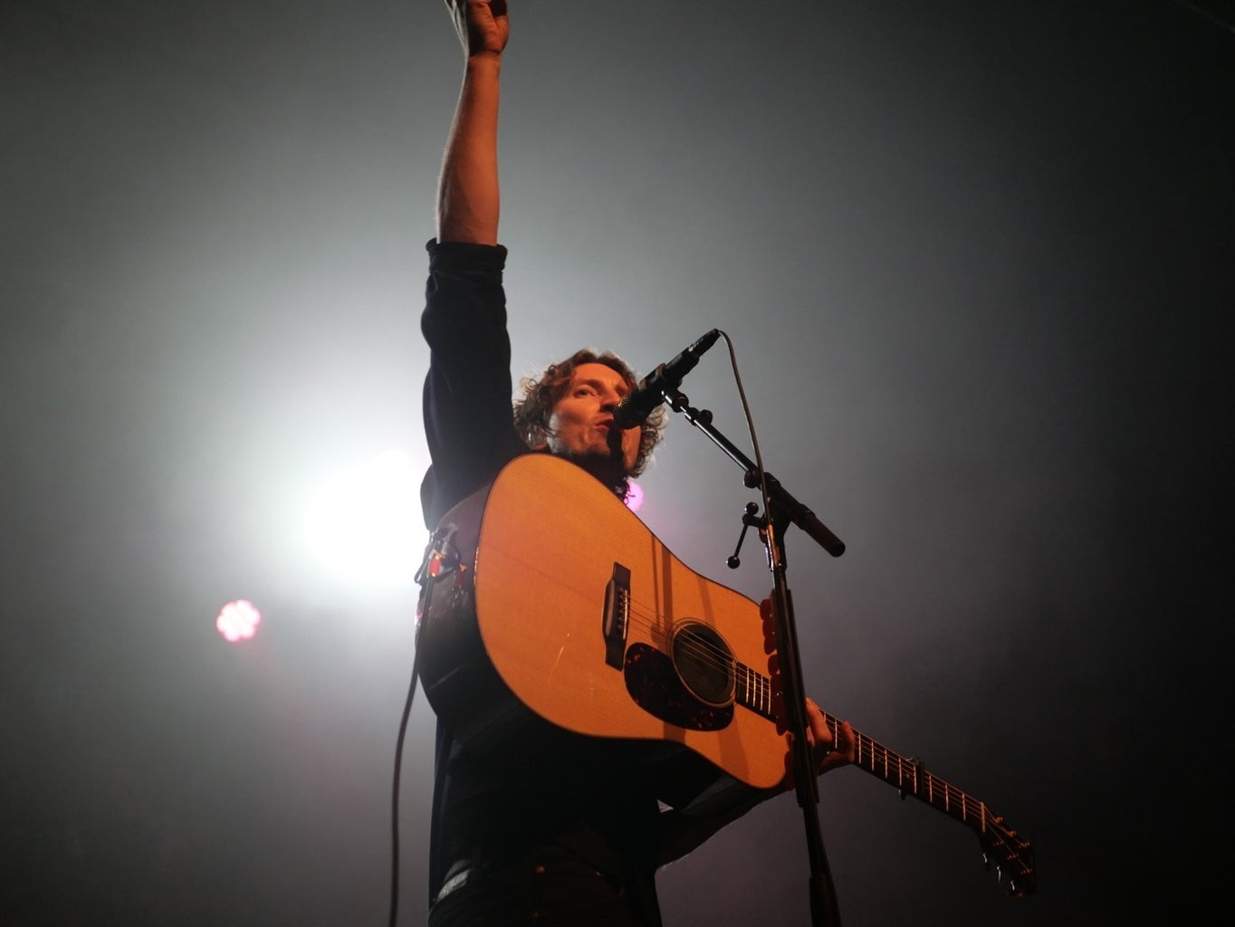 Man holding guitar with arm in the air at mic stand