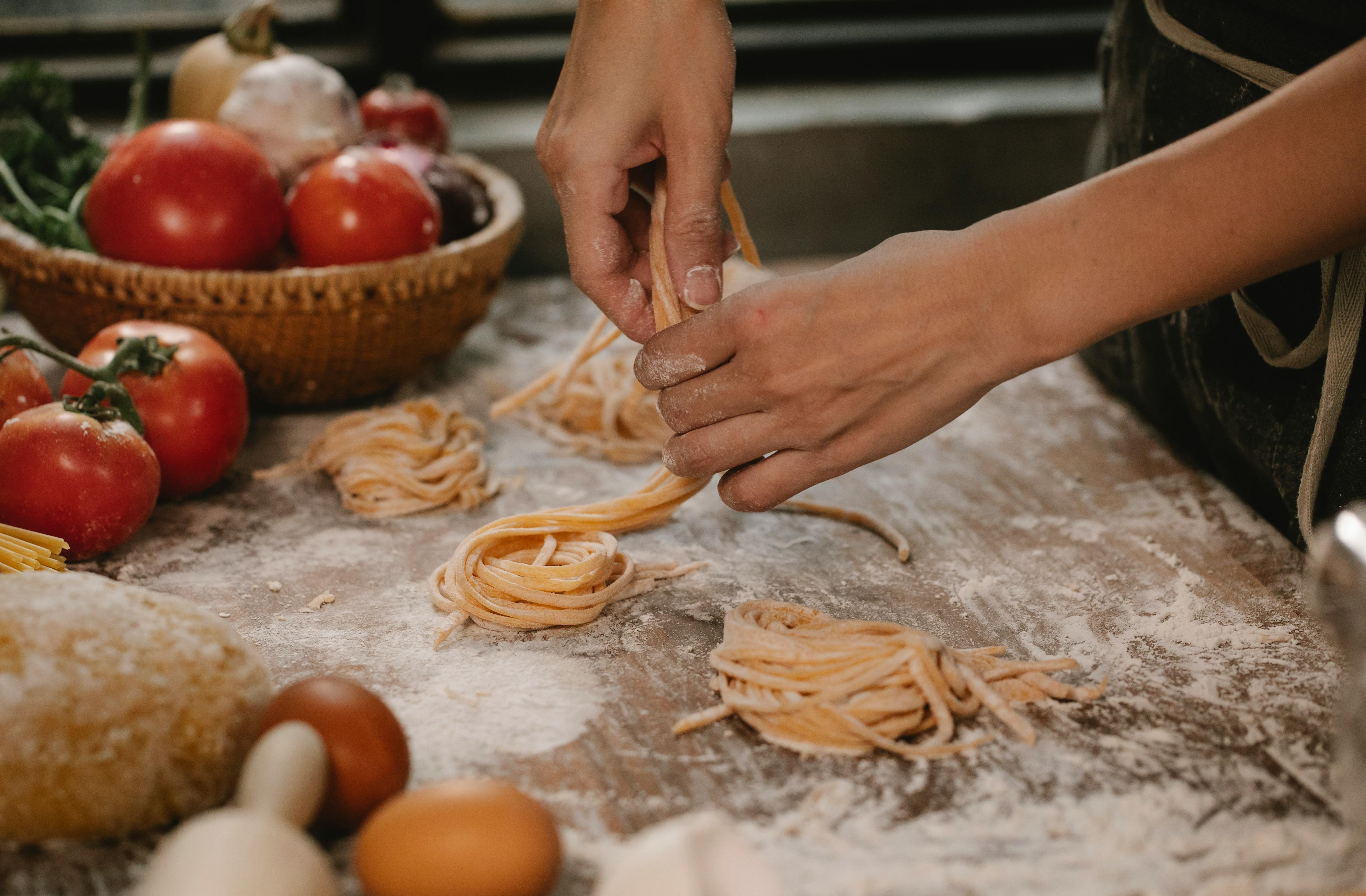 Fresh pasta on work surface with tomatoes in background.