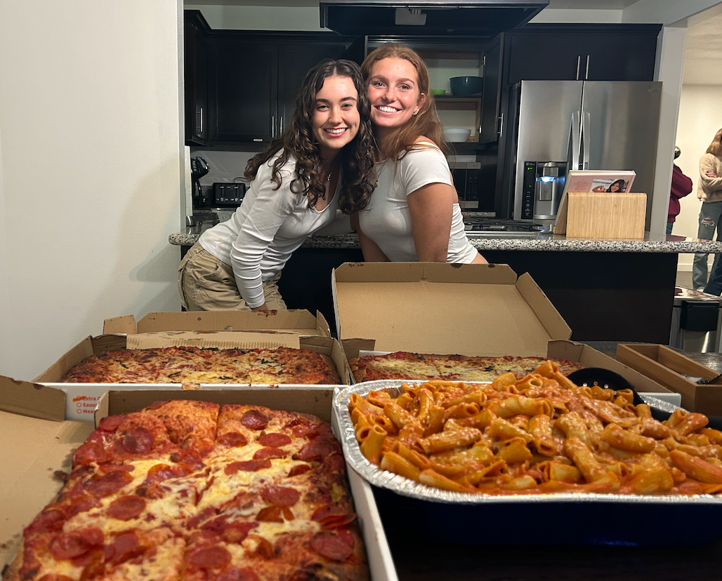 Two girls smiling in front of a table of Italian food.