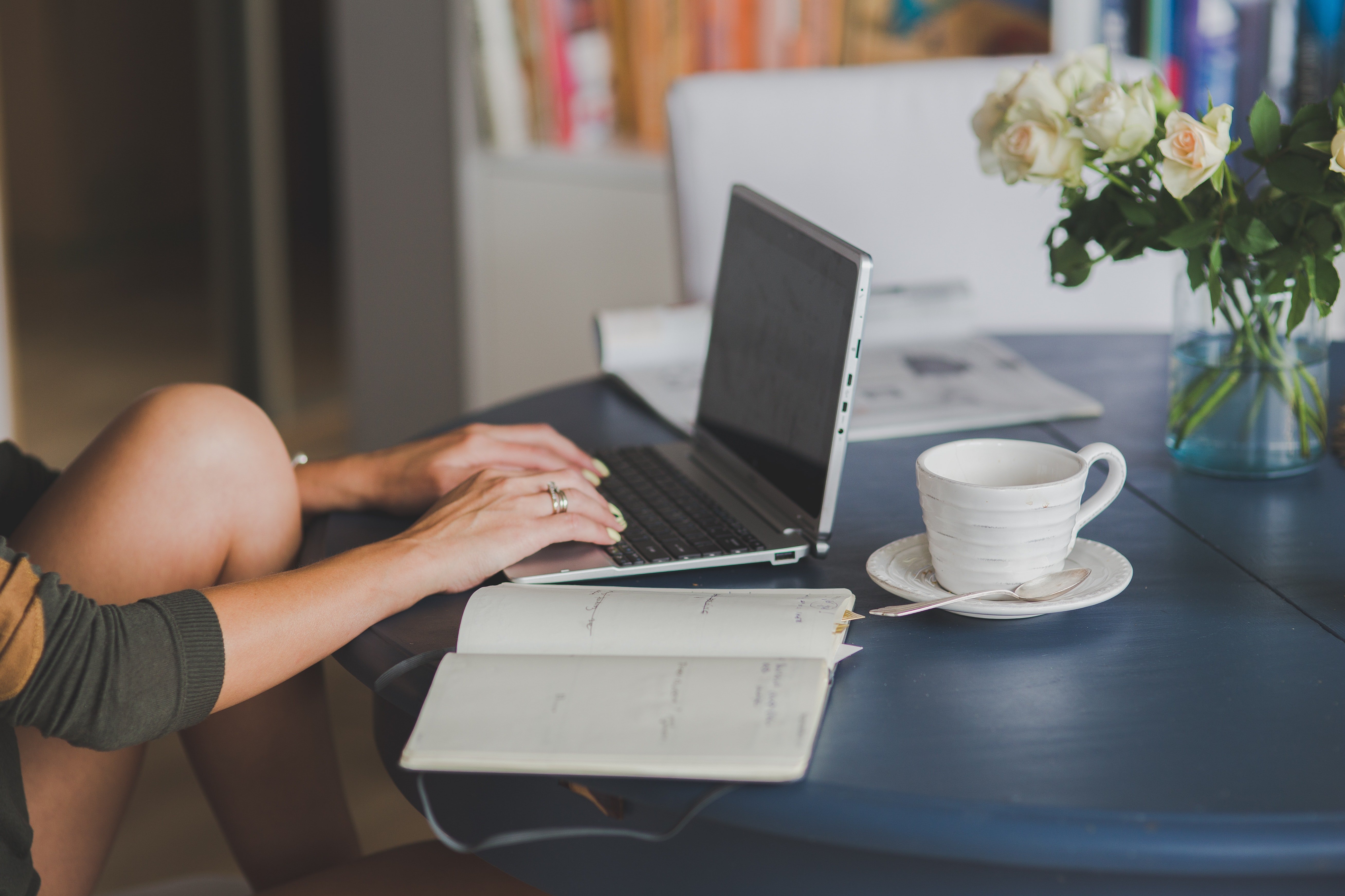 A woman works on a computer, and the table has a coffee cup and open notebook.