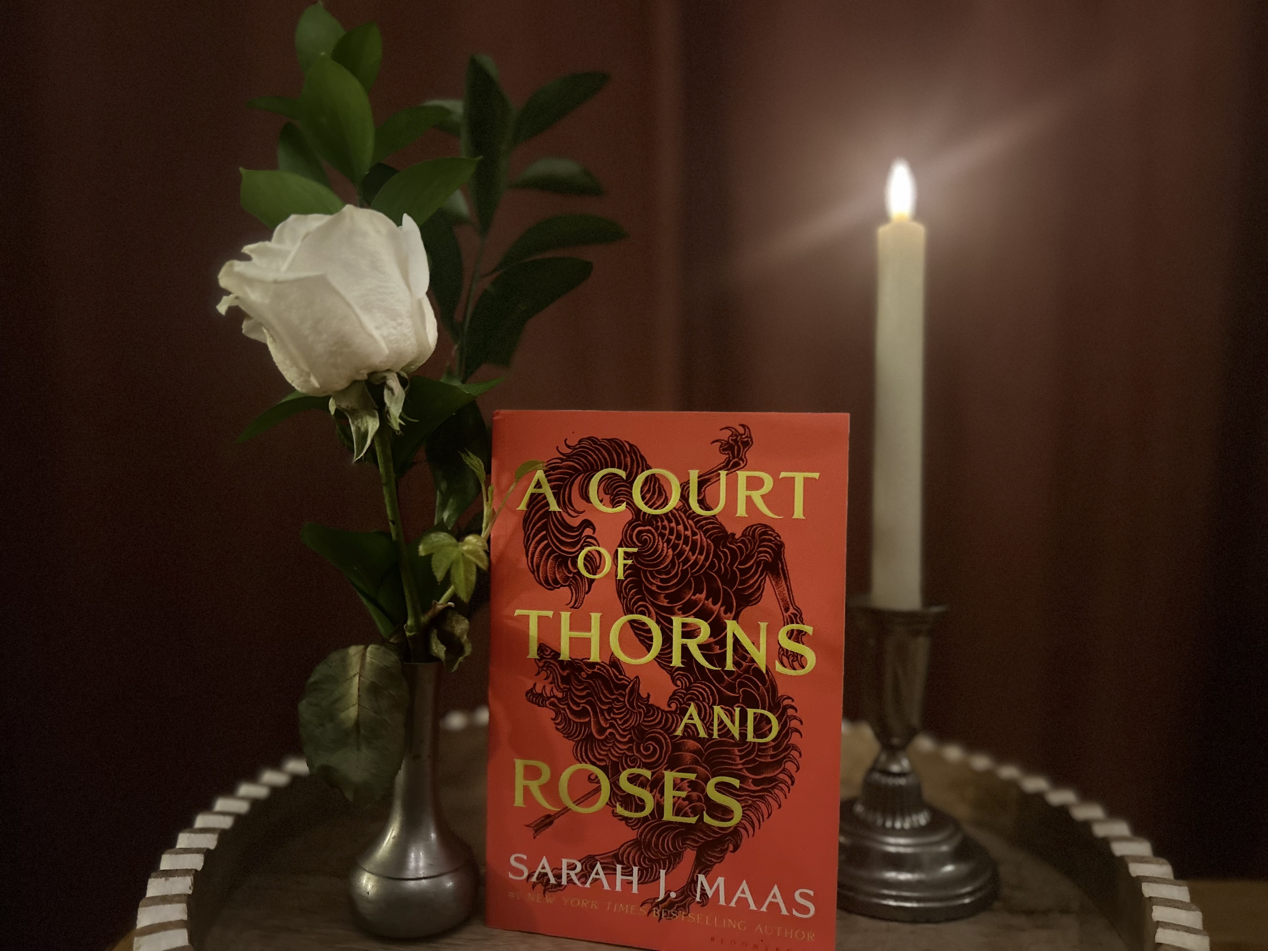 A Court of Thorns and Roses book with a candle and rose at its sides.