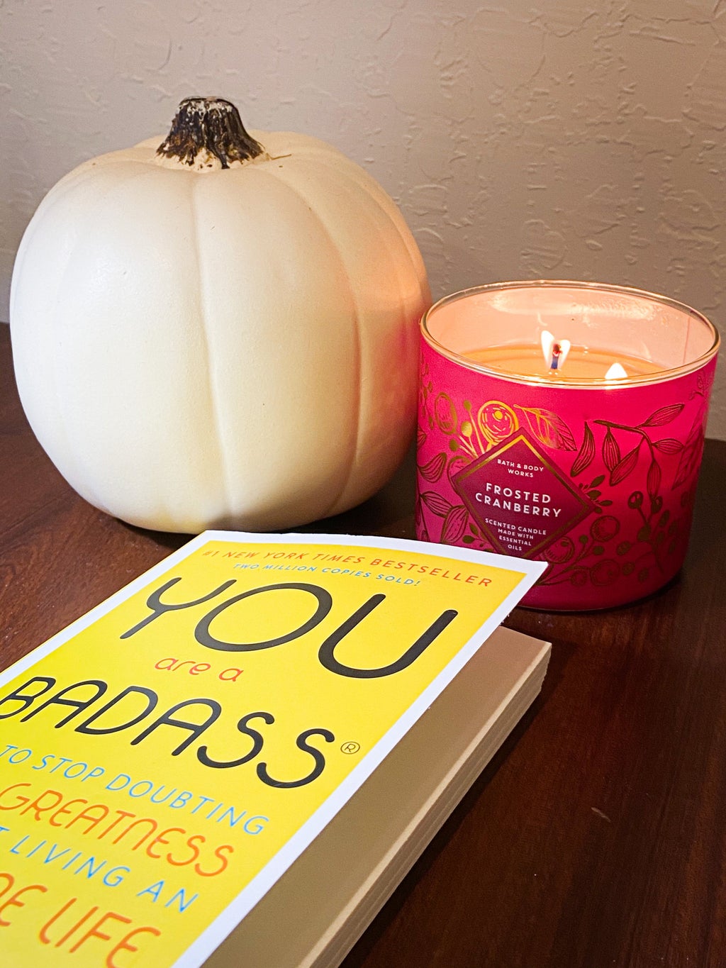 white pumpkin and lit pink candle with yellow book