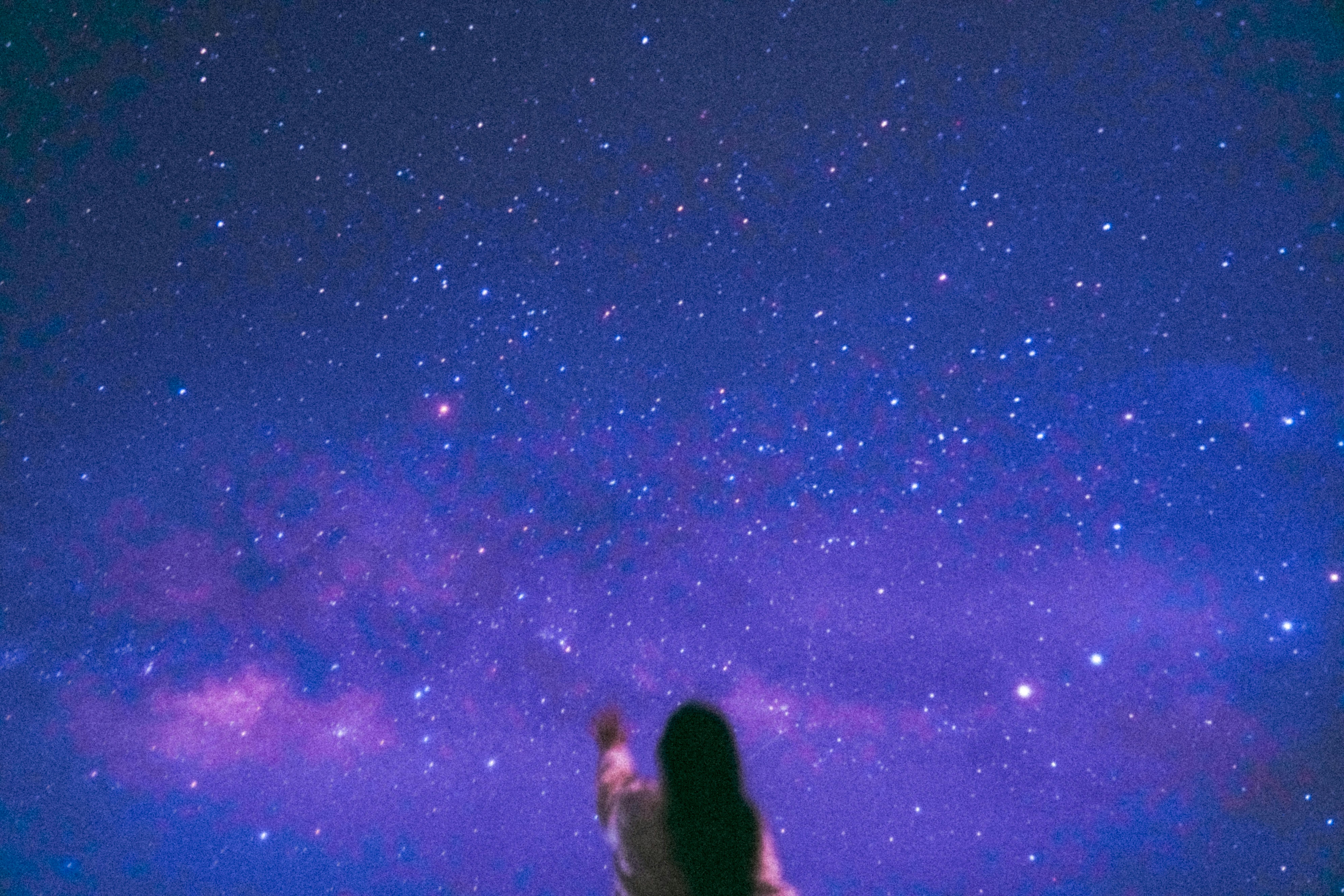 Woman reaching her hand out to purple and blue sky with stars