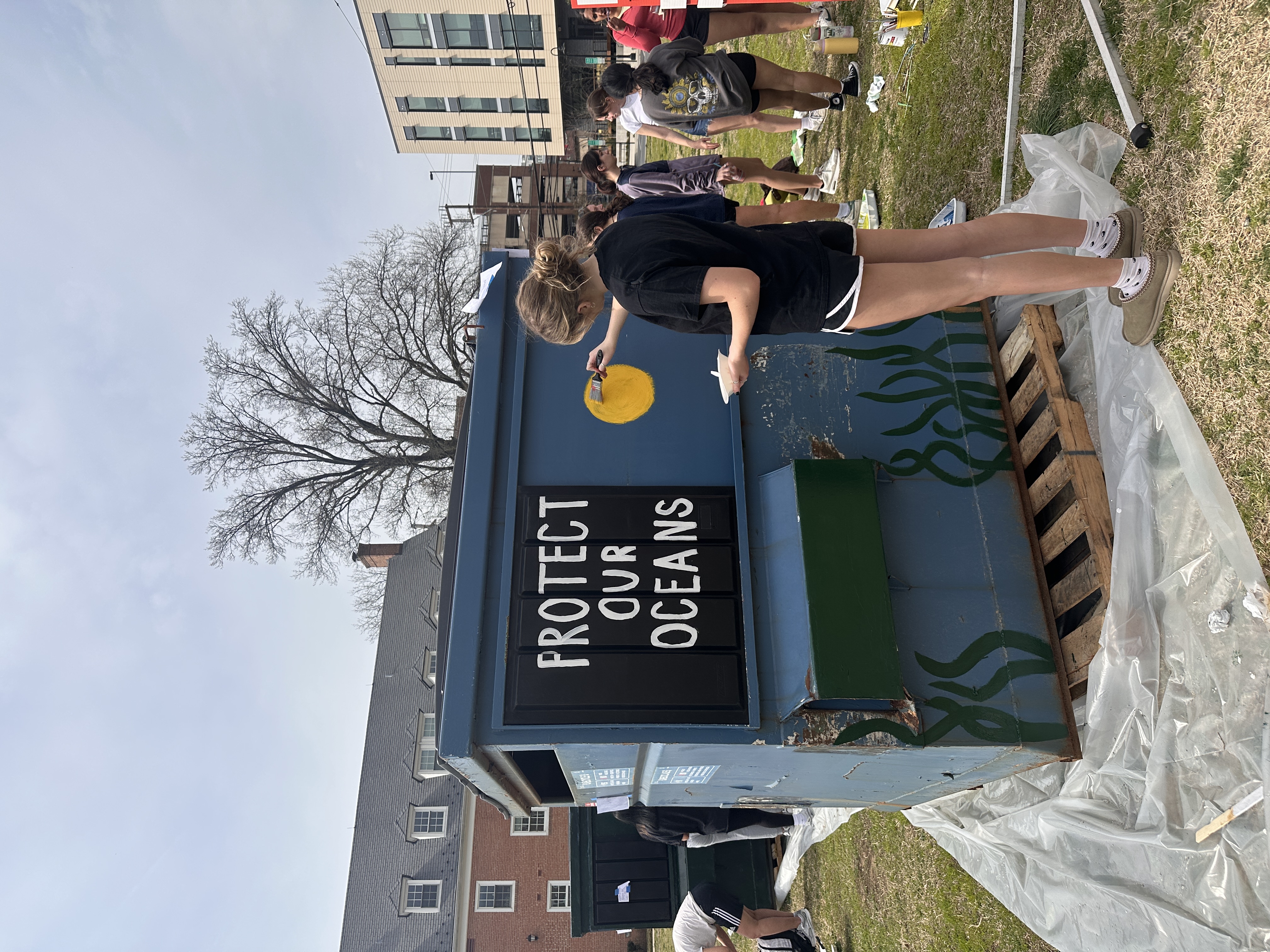 Woman painting a sun on a dumpster.