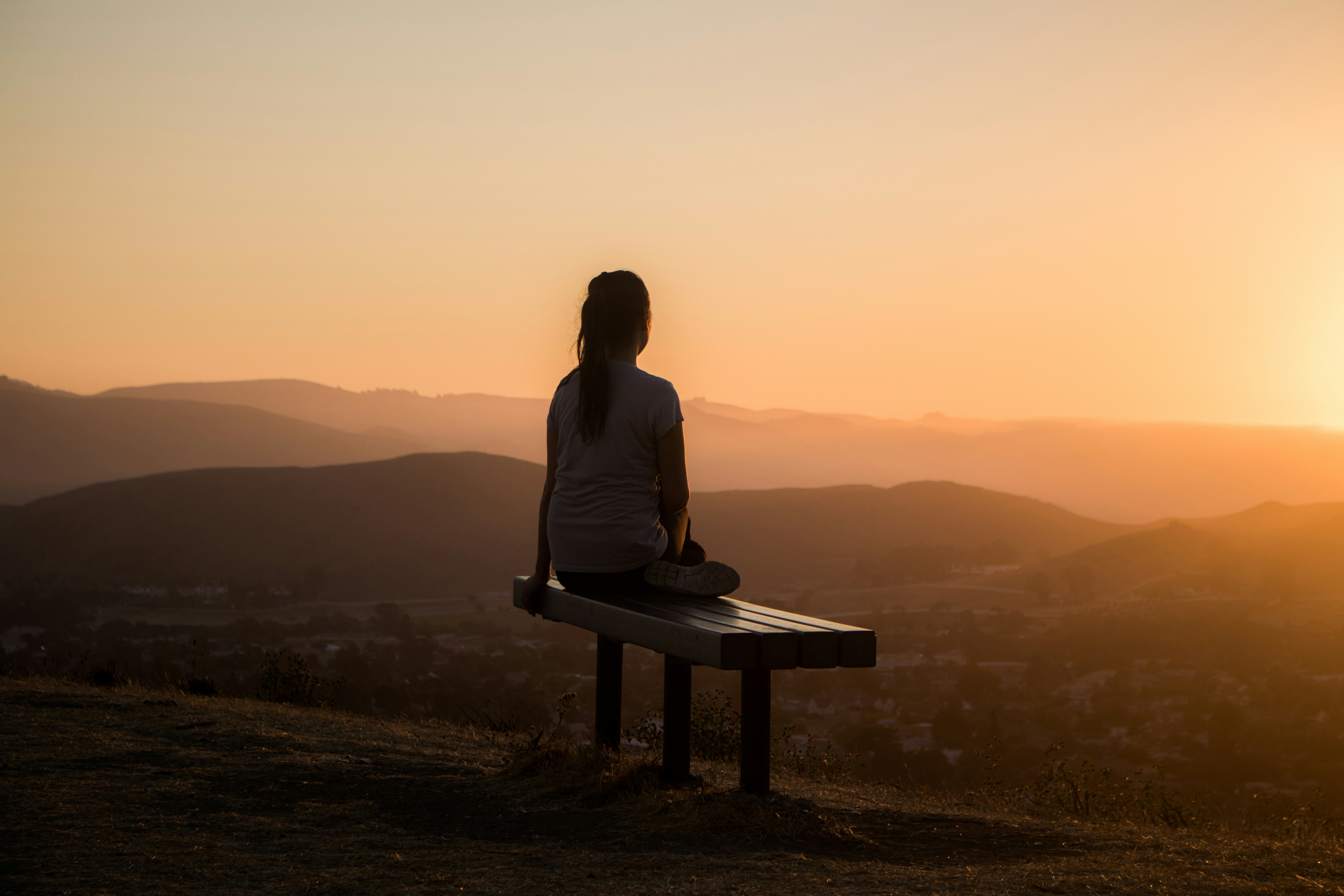 woman sitting on a bench looking at a scenic sunset