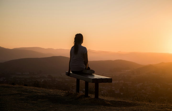 woman sitting on a bench looking at a scenic sunset