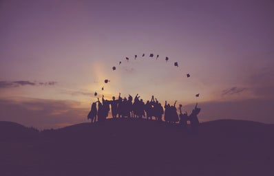 People throwing their graduation caps against a sunset