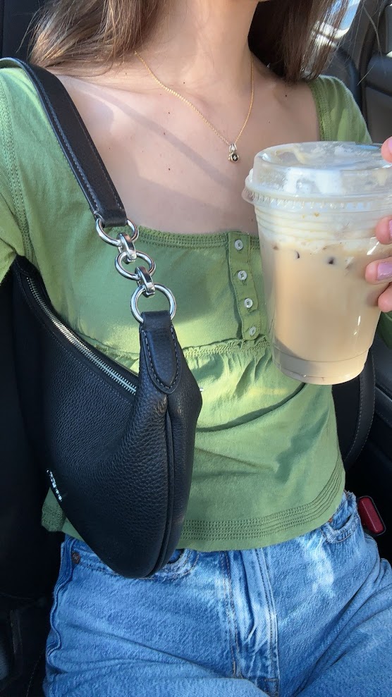 A woman wearing green holds an iced latte and a purse while sitting in a car.