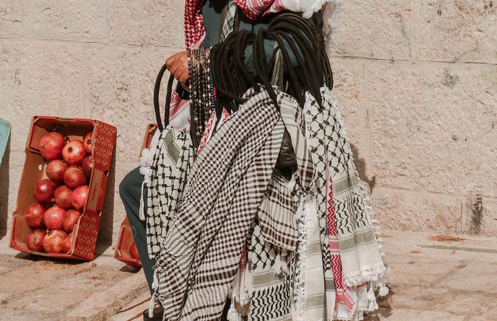 Man holding a variety of kuffiyeh scarves on his wrist.