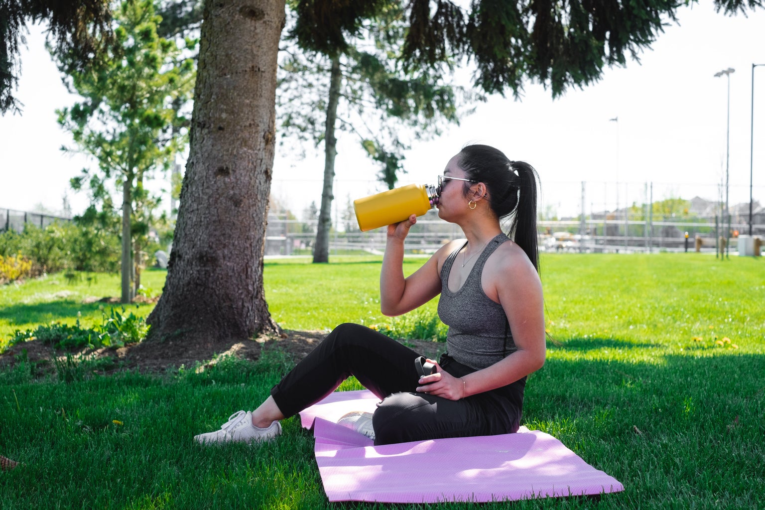 woman-drinks-from-a-yellow-water-bottle-under-a-tree
