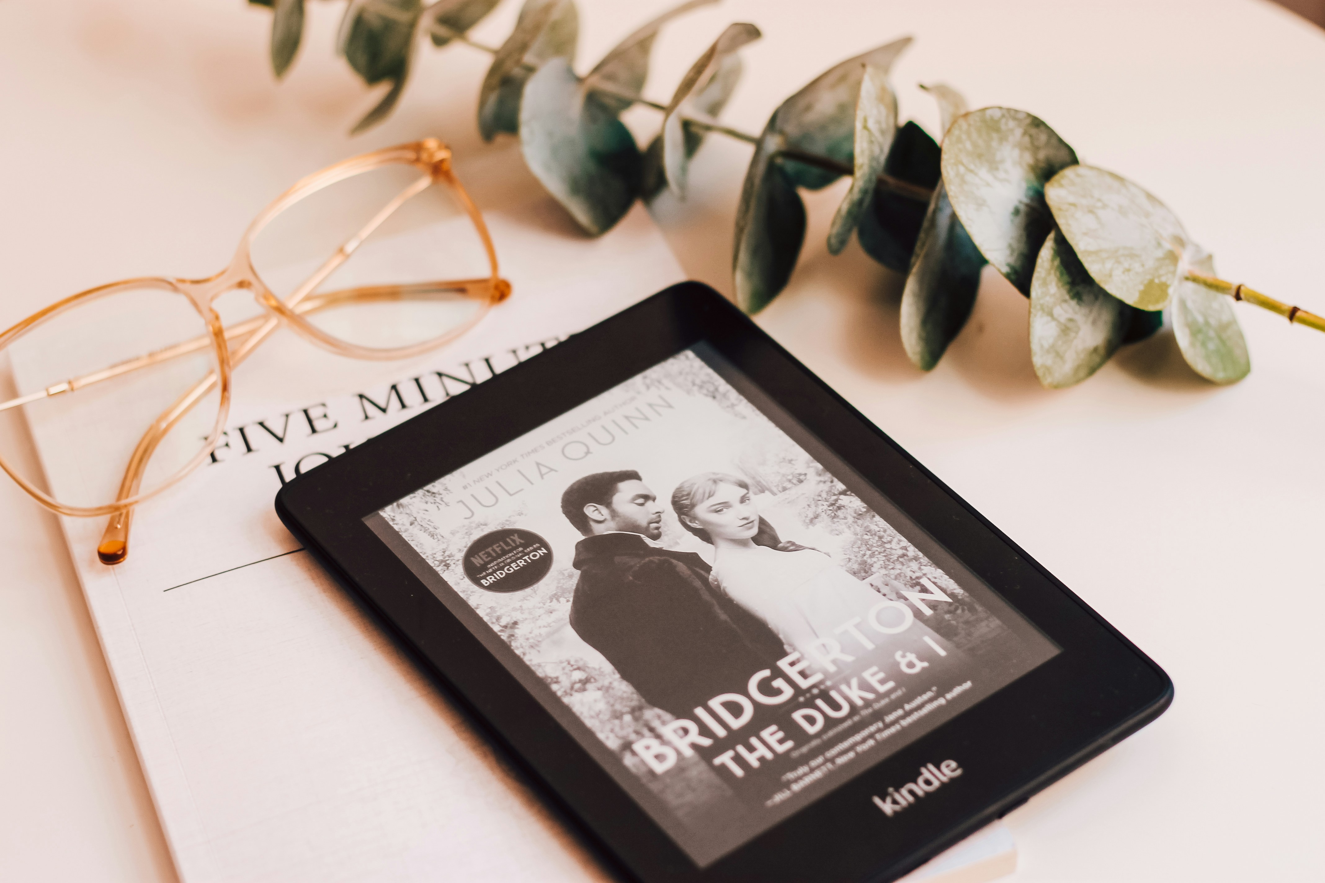 First Bridgerton book on a black kindle with a plant and glasses.