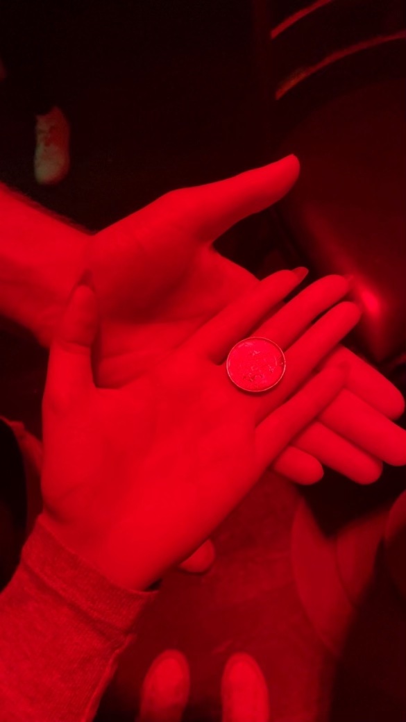 Two hands hold coin under red light
