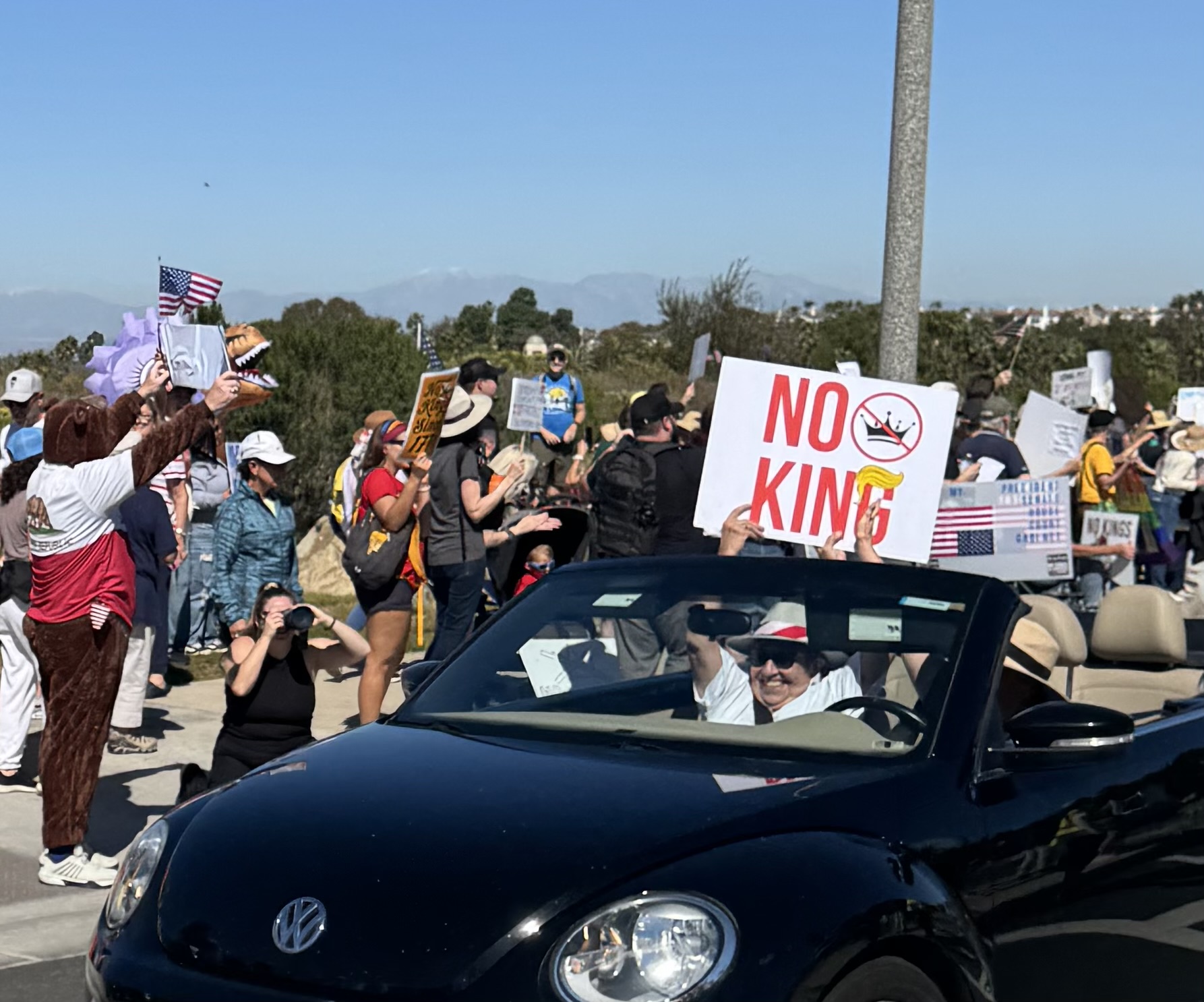 As the car approaches ‘No Kings’ protesters, the passenger holds up a sign in support of the rally held Oct. 18.