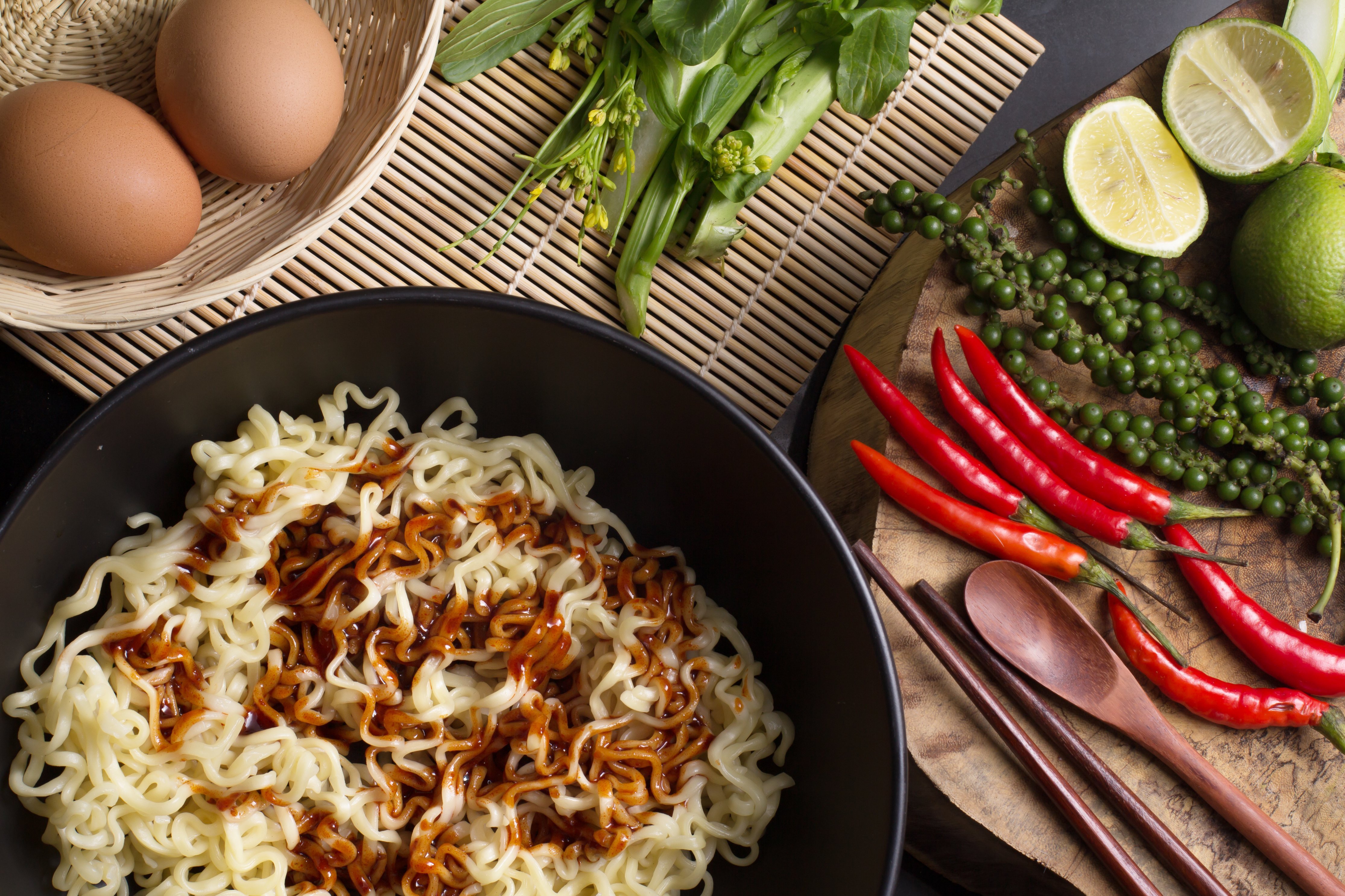 Ramen in a pan with sauce, and eggs and vegetables on the counter.