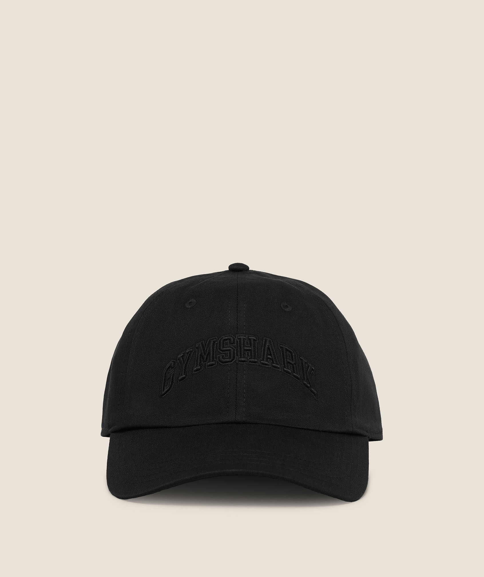 A black baseball cap with a curved brim and subtle raised black lettering on the front, photographed against a plain beige background for a clean, understated look.