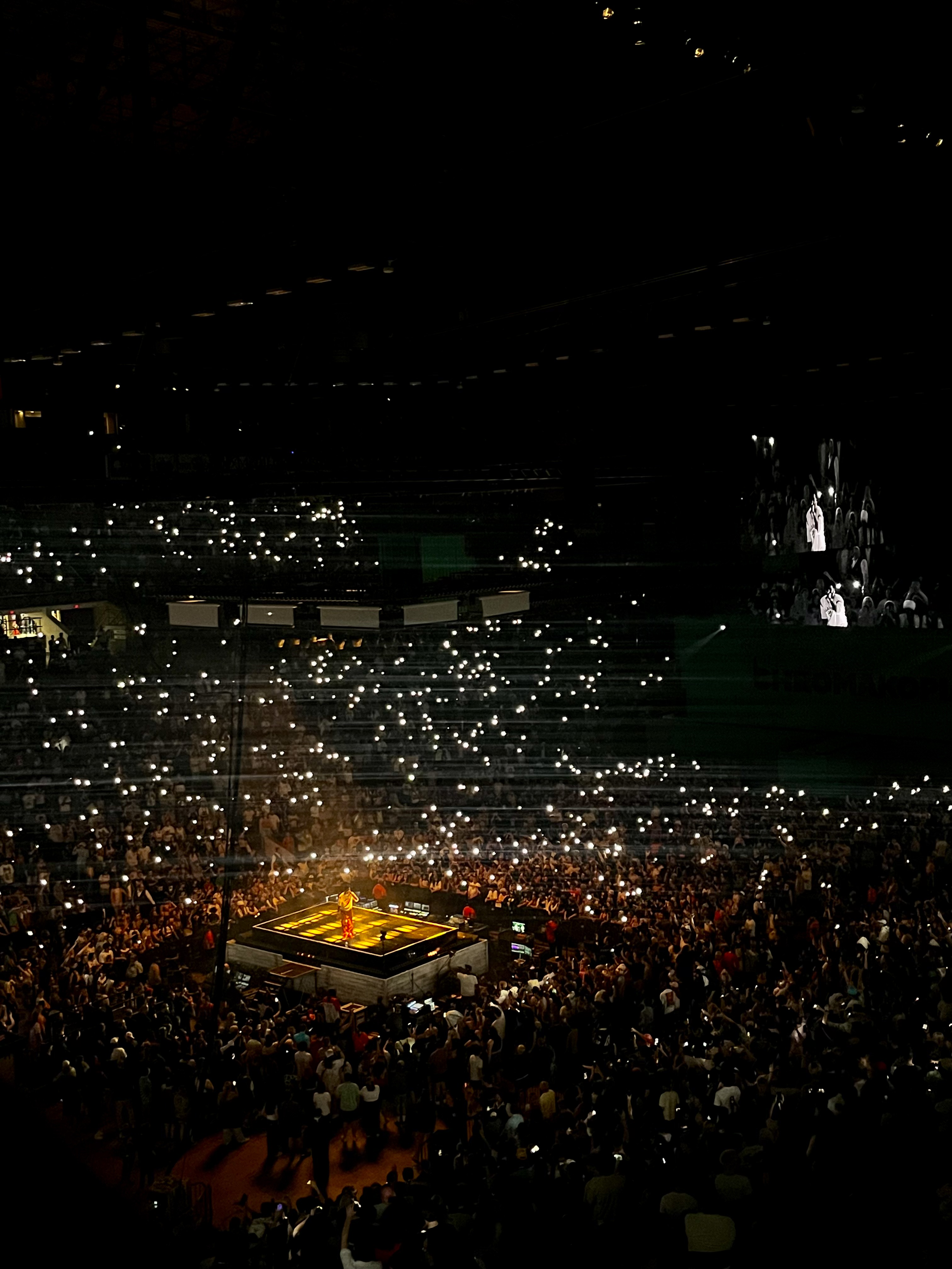 A concert with hundreds of phone flashlights illuminating the crowd and creating a star effect