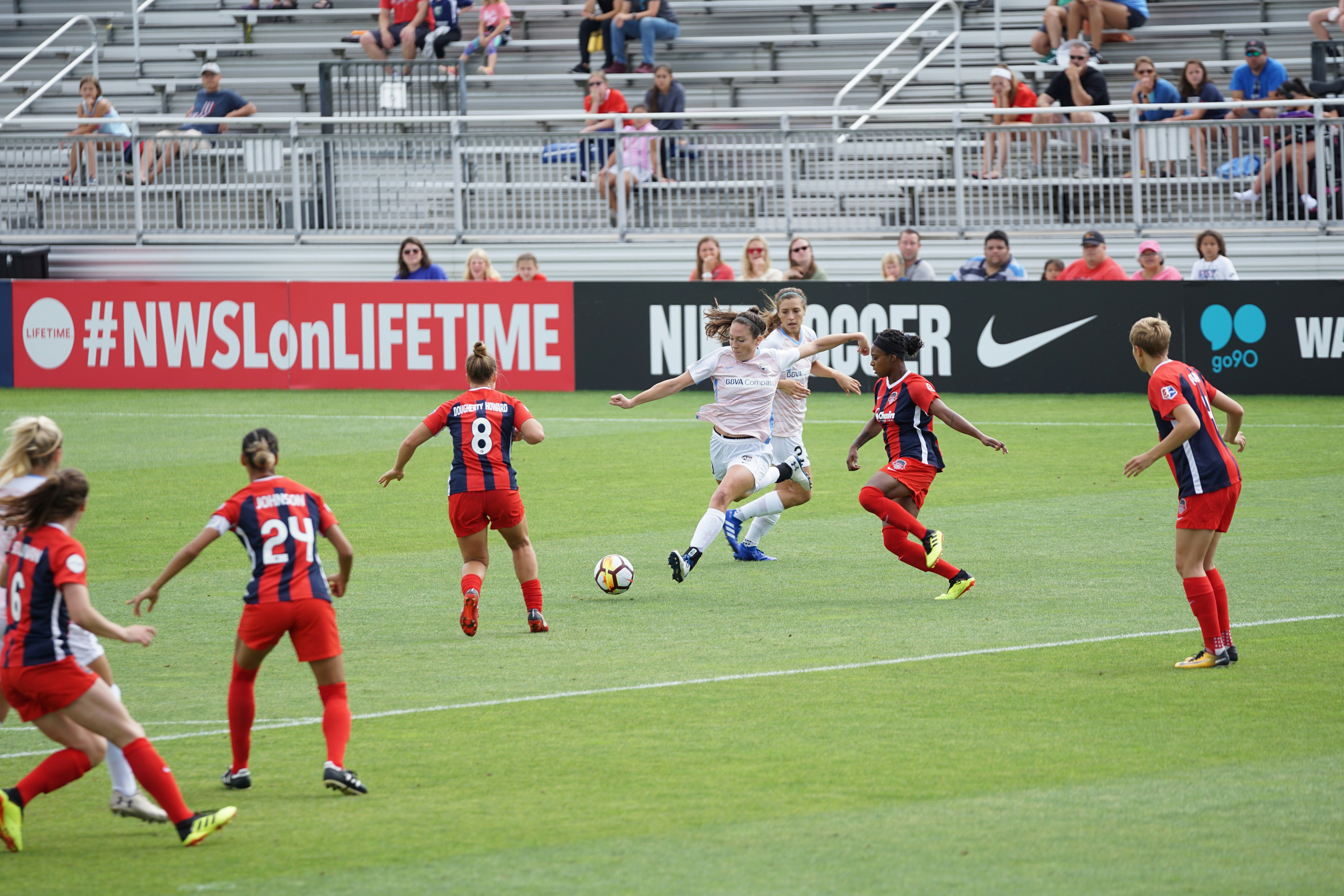Soccer player kicking ball with other players around her