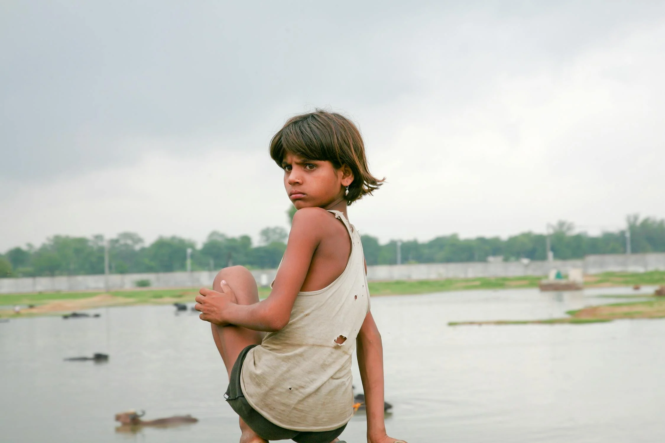 A girl in tank top sitting near a lake while looking afar