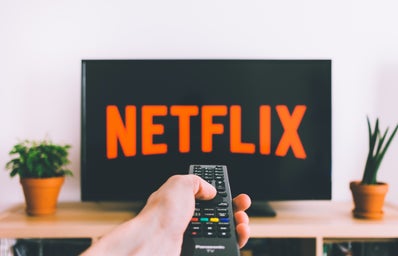 hand holding remote with Netflix on TV screen