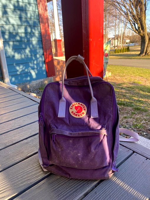 purple fjallraven kanken backpack on a porch with sunlight beams.