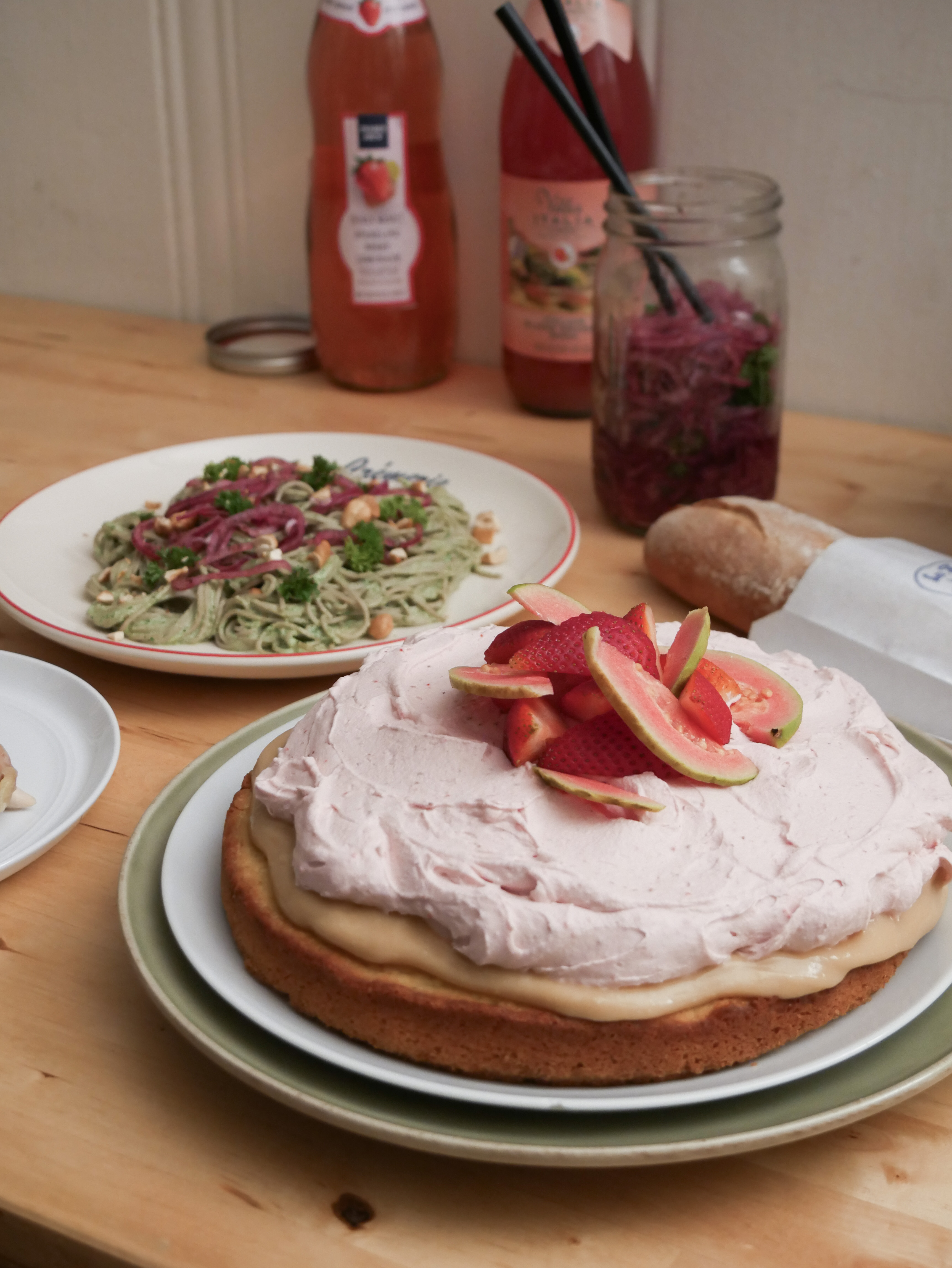 Picture of cake with noodles, bread, onions and drinks in the background