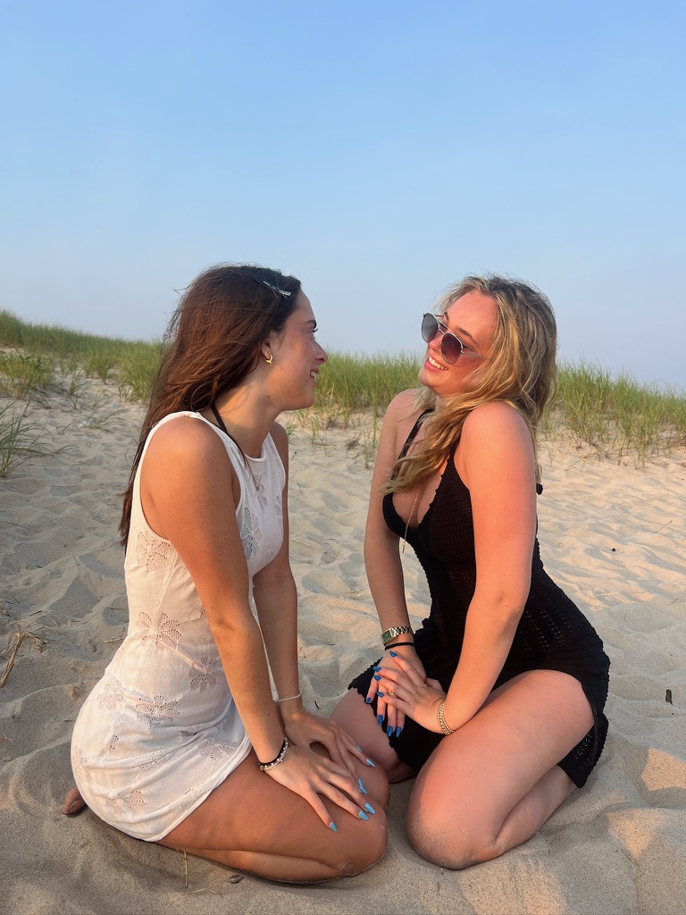 Two women smiling on a beach dune.