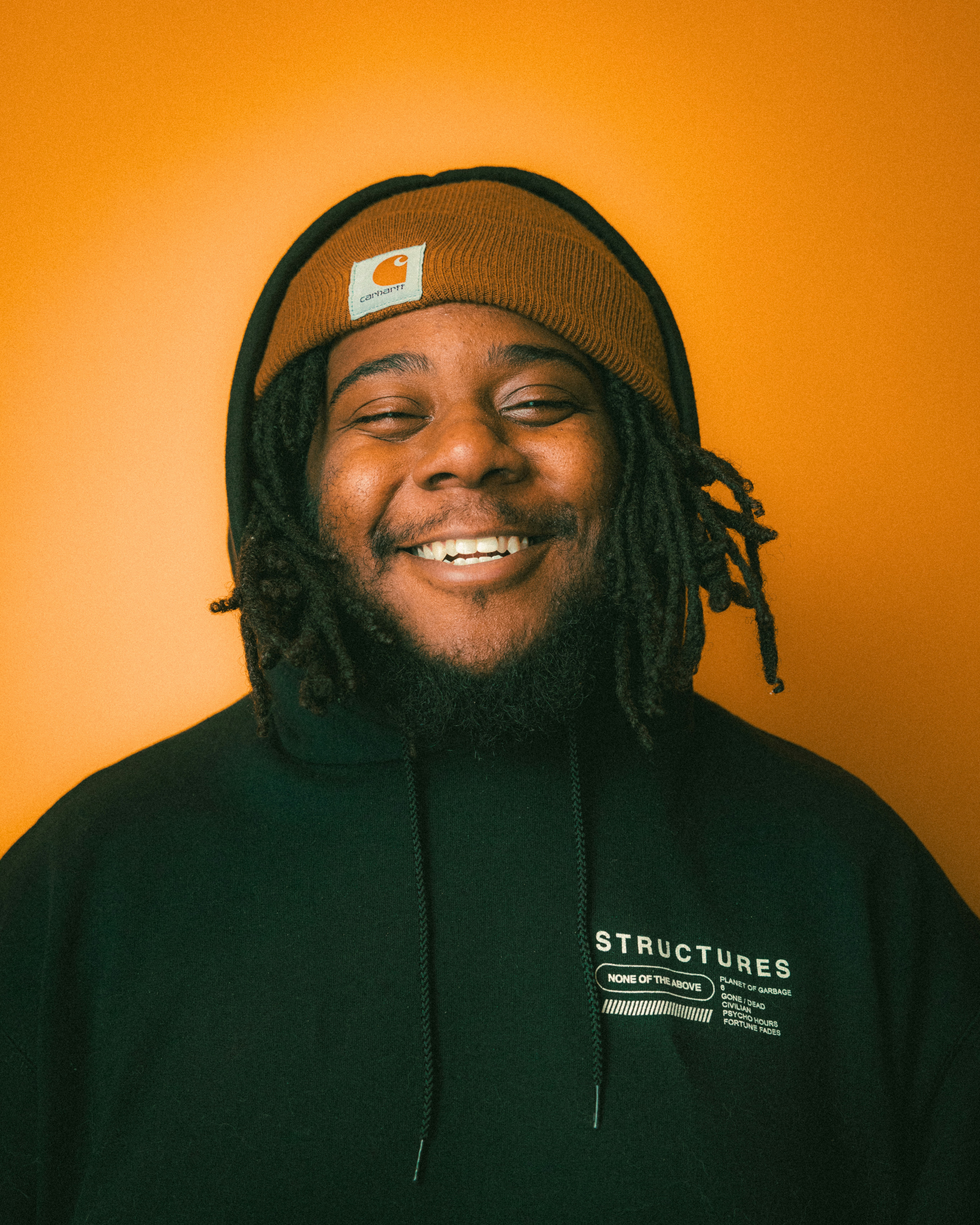 man smiling wearing carhartt toque on an orange background