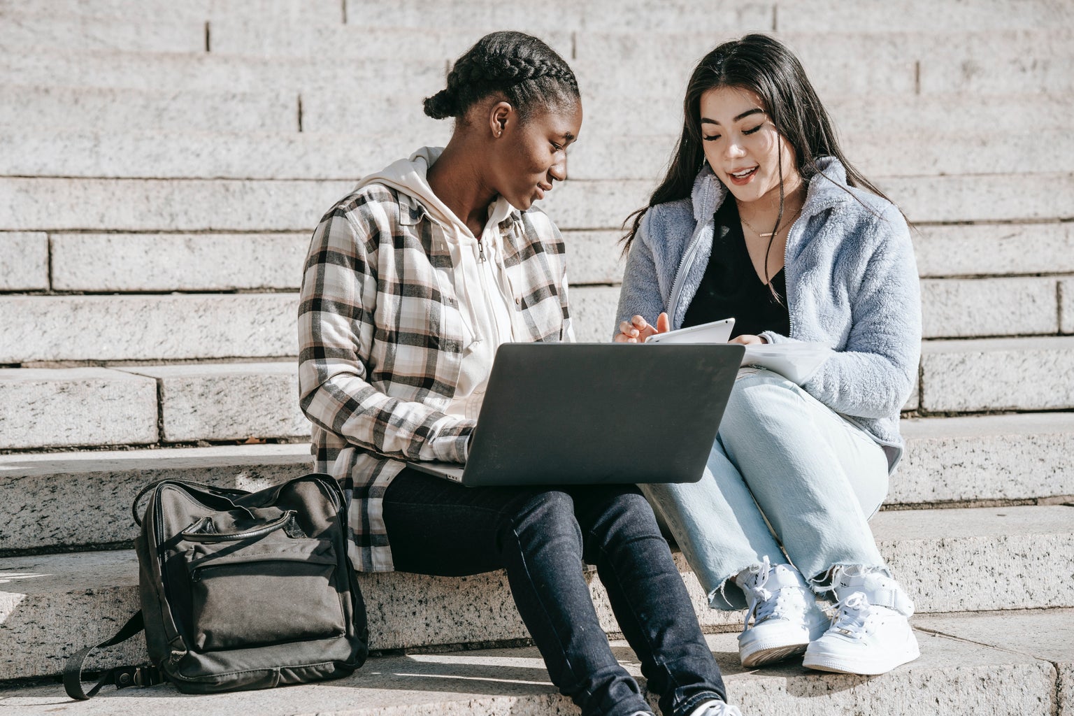 two people sitting on stairs looking at a laptop