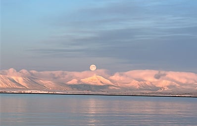 A landscape shot of the Iceland horizon. It captures the moon over some glaciers in the background.