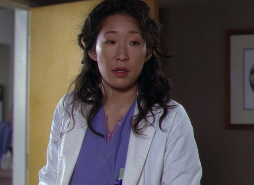 Girl with black hair wearing a white lab coat and blue scubs.