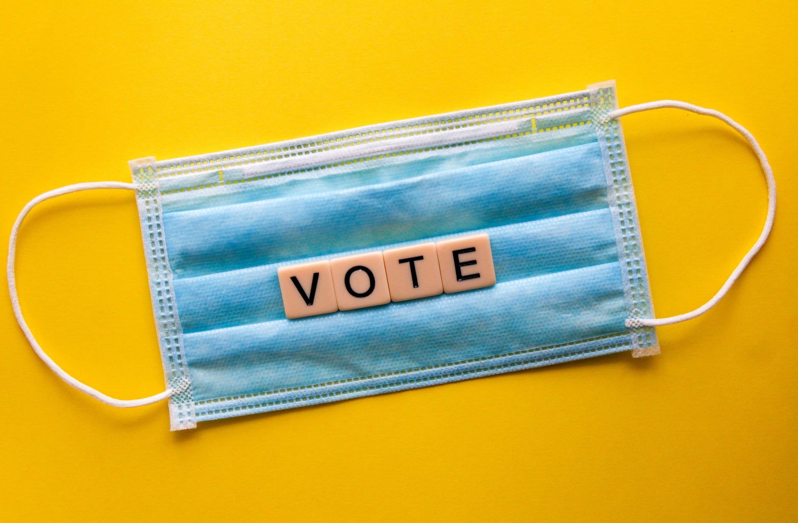 blue mask with tiles spelling "vote" in front of yellow background.
