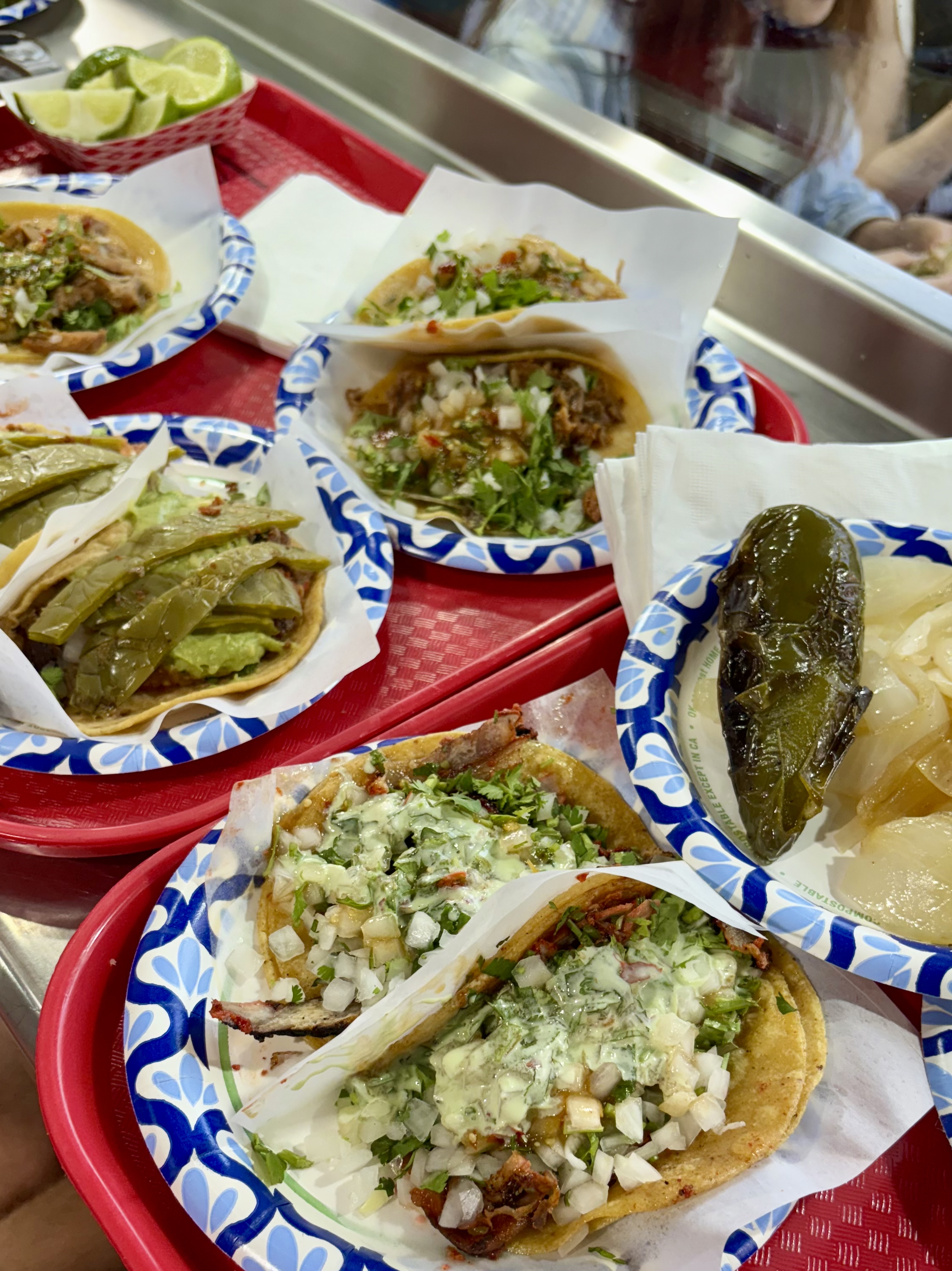 Close-up of multiple tacos from Tacos El Gordo on a red serving tray, including Adobada, Azteca, and Suadero.