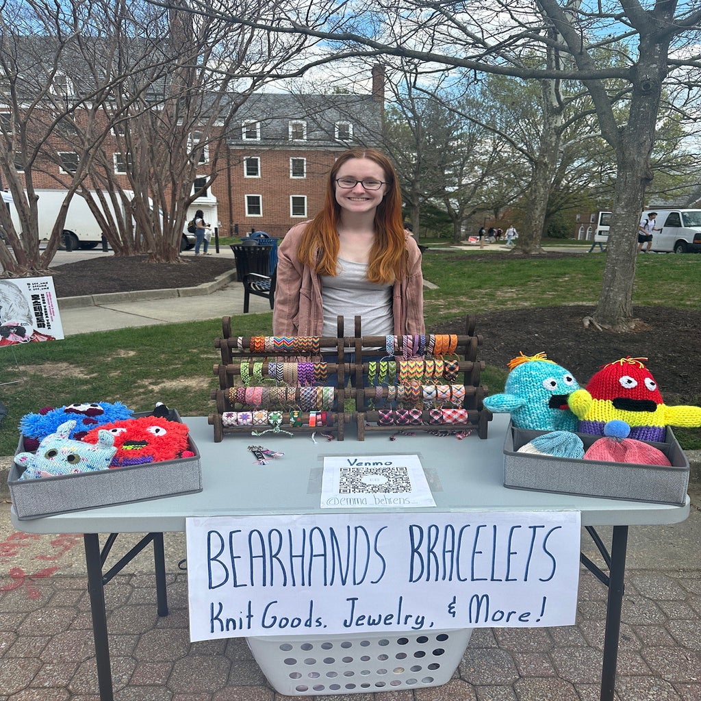 Emma Behrens poses with her knit goods and friendship bracelets at the BearHands Bracelets table.