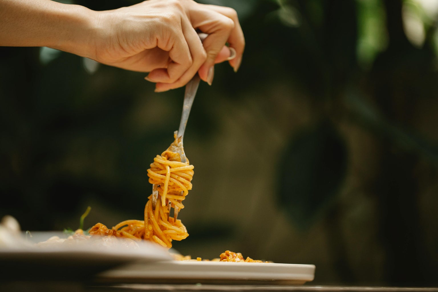 Hand twirling spaghetti on a fork over a plate of pasta.