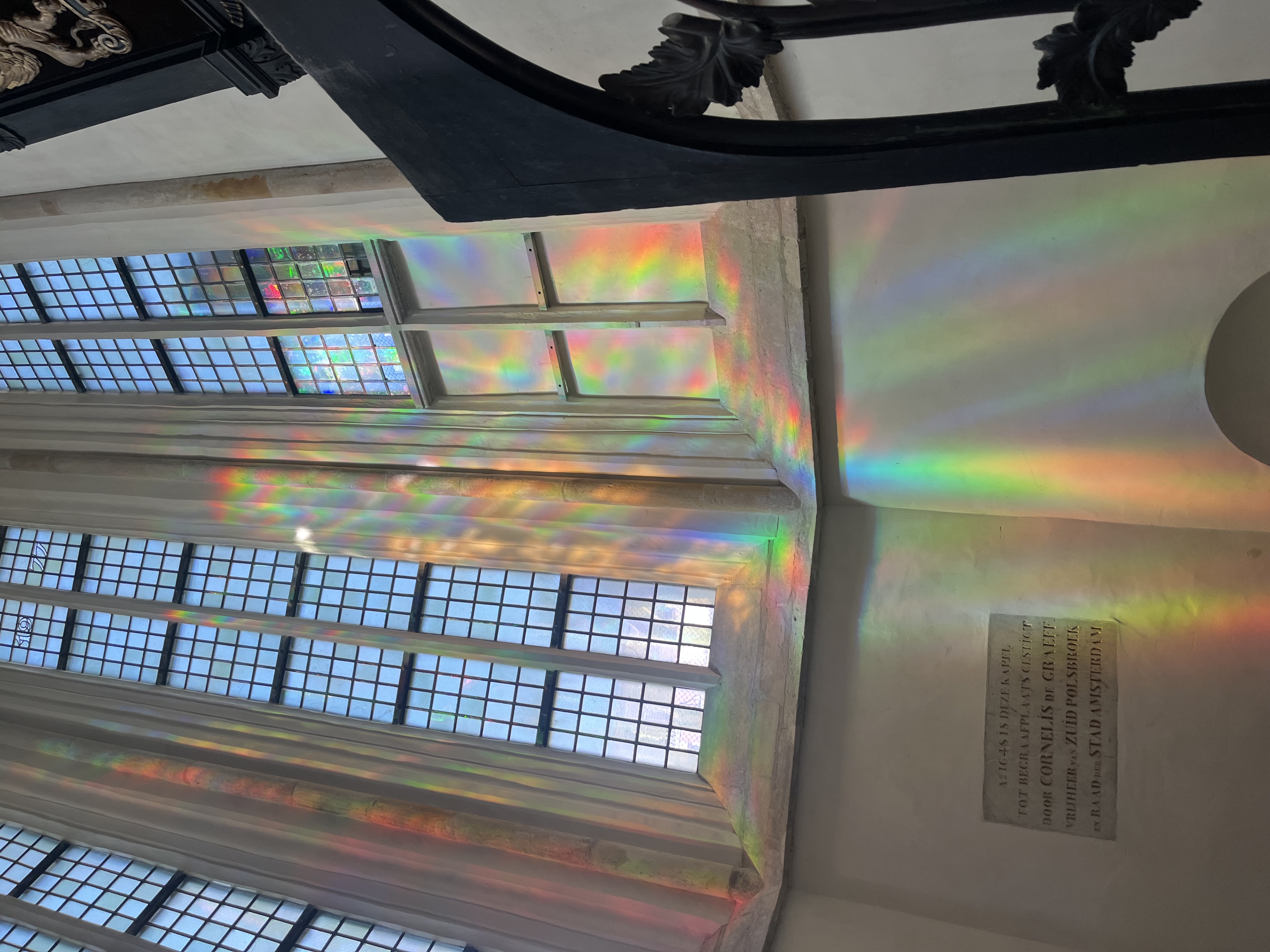 A tall window of an ancient church building in Europe with rainbow flares across the wall