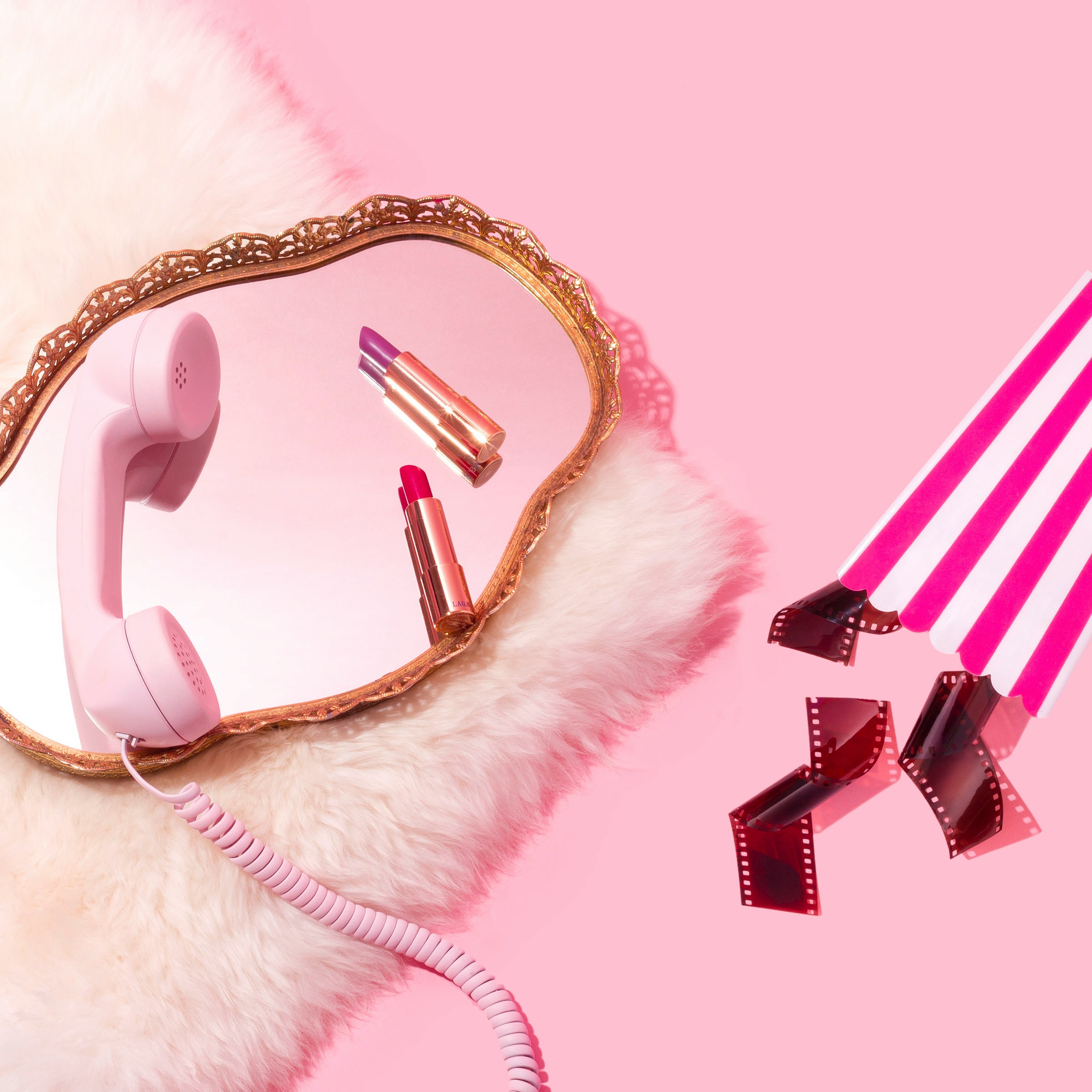 pink background, fuzzy rug with mirror and cable phone, lipsticks, popcorn box and film reels