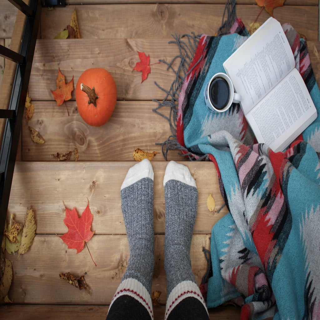 Person wearing socks on a deck with a pumpkin and drinks and a blanket