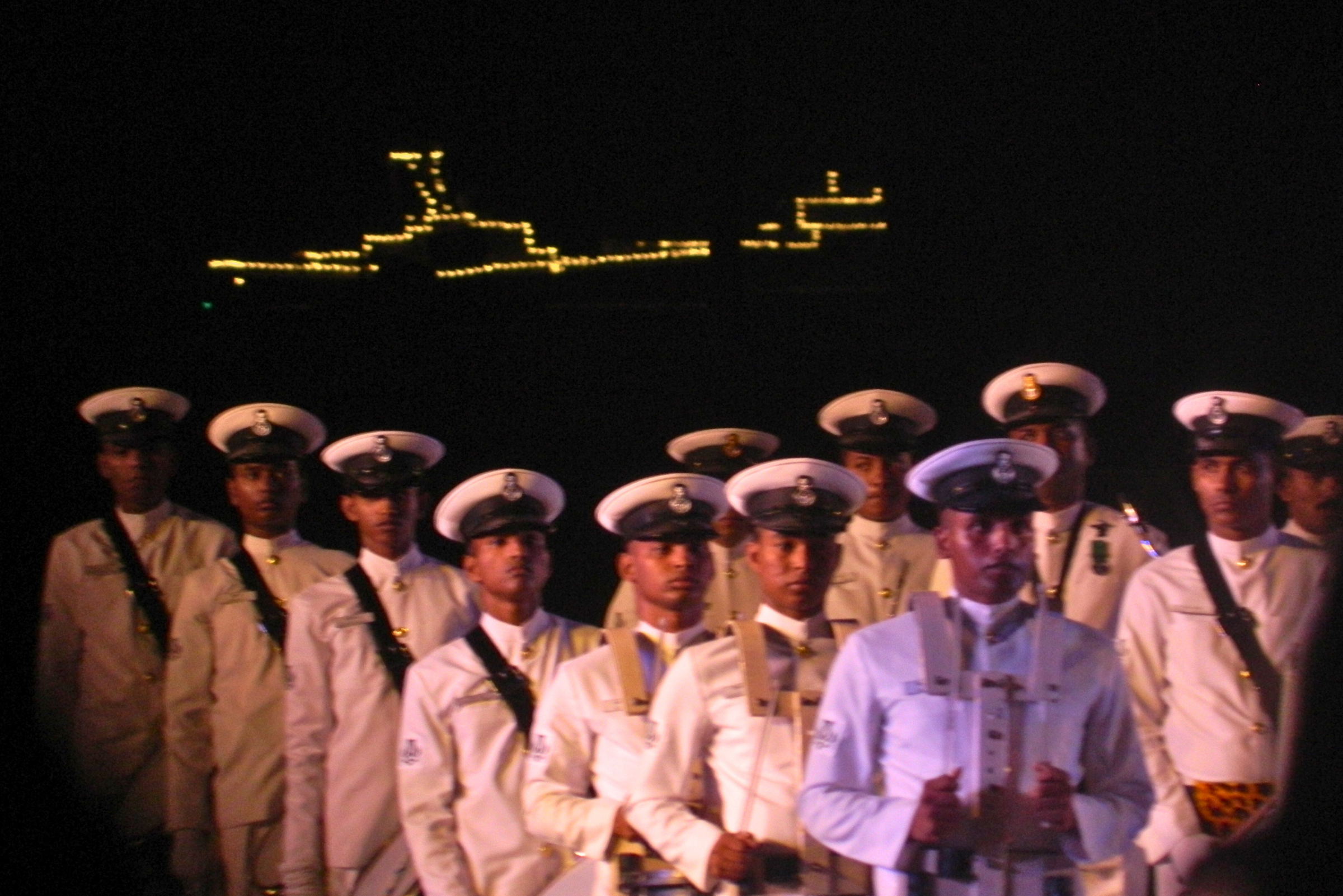 Ships lit up with lights and personnel standing at shore.