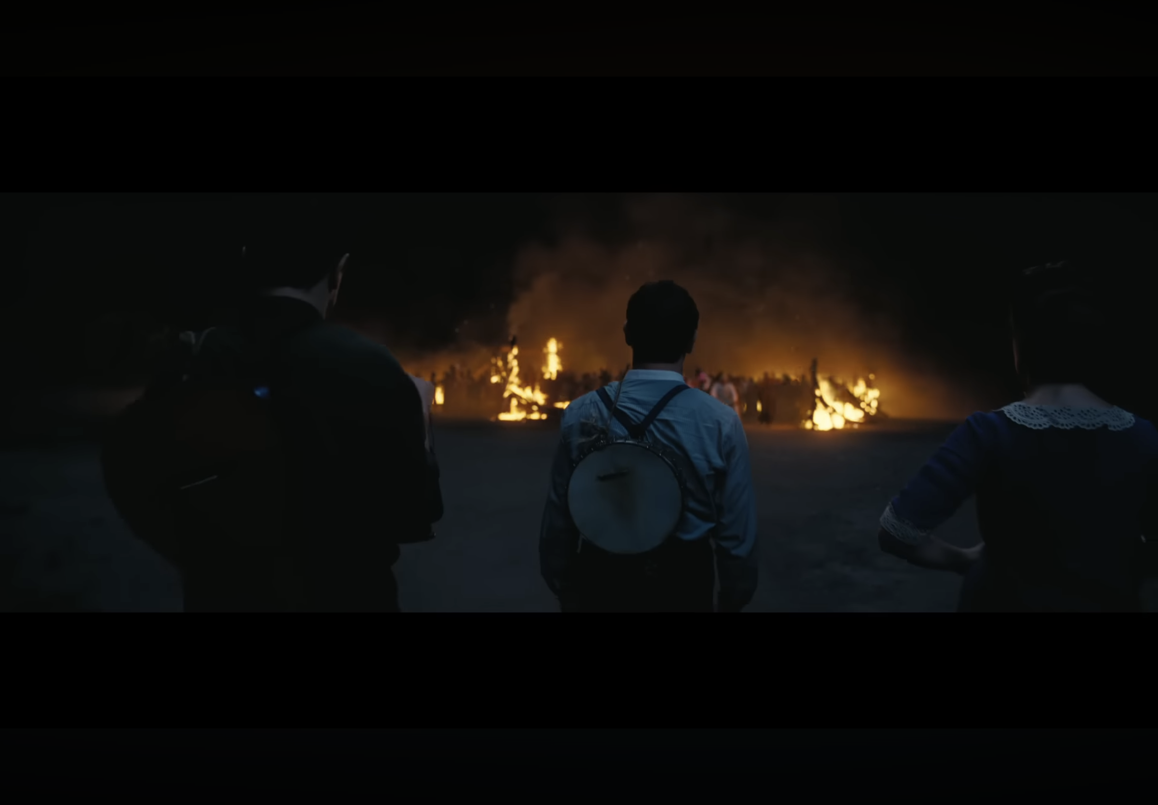 three people stand looking at a fire from the movie Sinners
