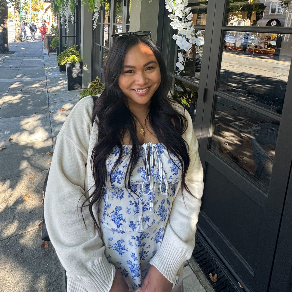 woman with long, dark hair posing on the street wearing a white cardigan and blue and white floral dress