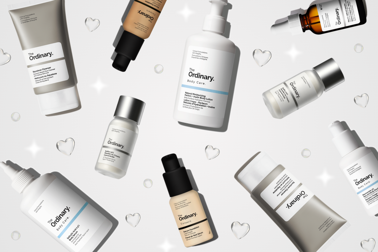 Scattered skincare products from The Ordinary against a light background, featuring various bottles and tubes. Small hearts add a playful touch.