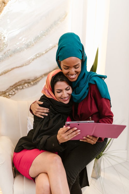 women in hijab reading together and smiling