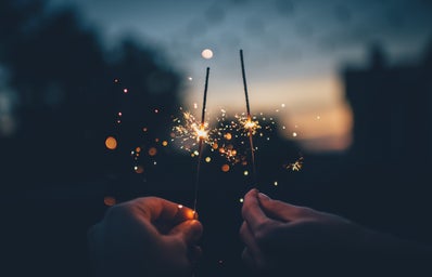 two hands holding sparklers with a sunset background