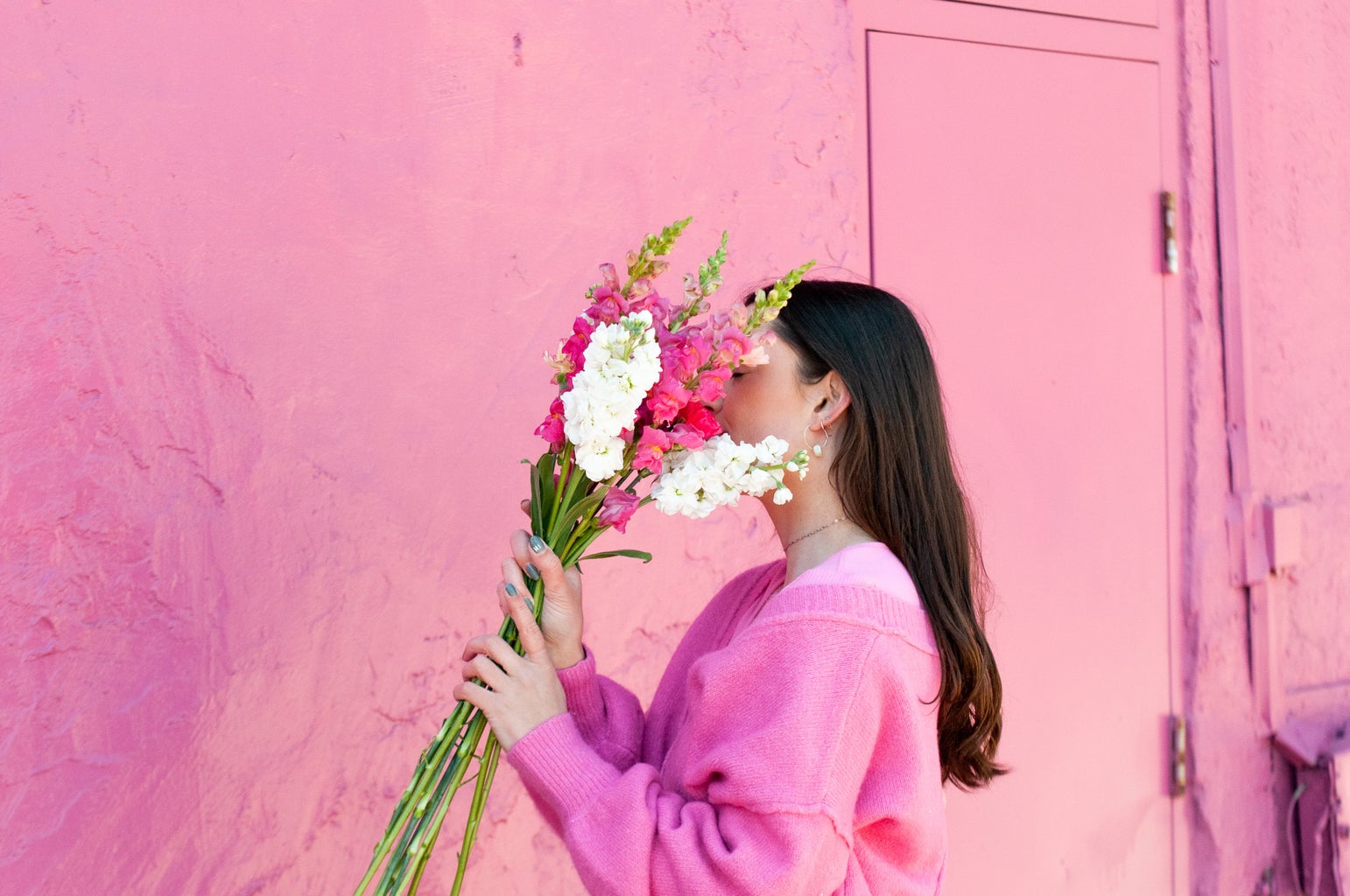 girl holding flowers to her face while wearing pink sweater