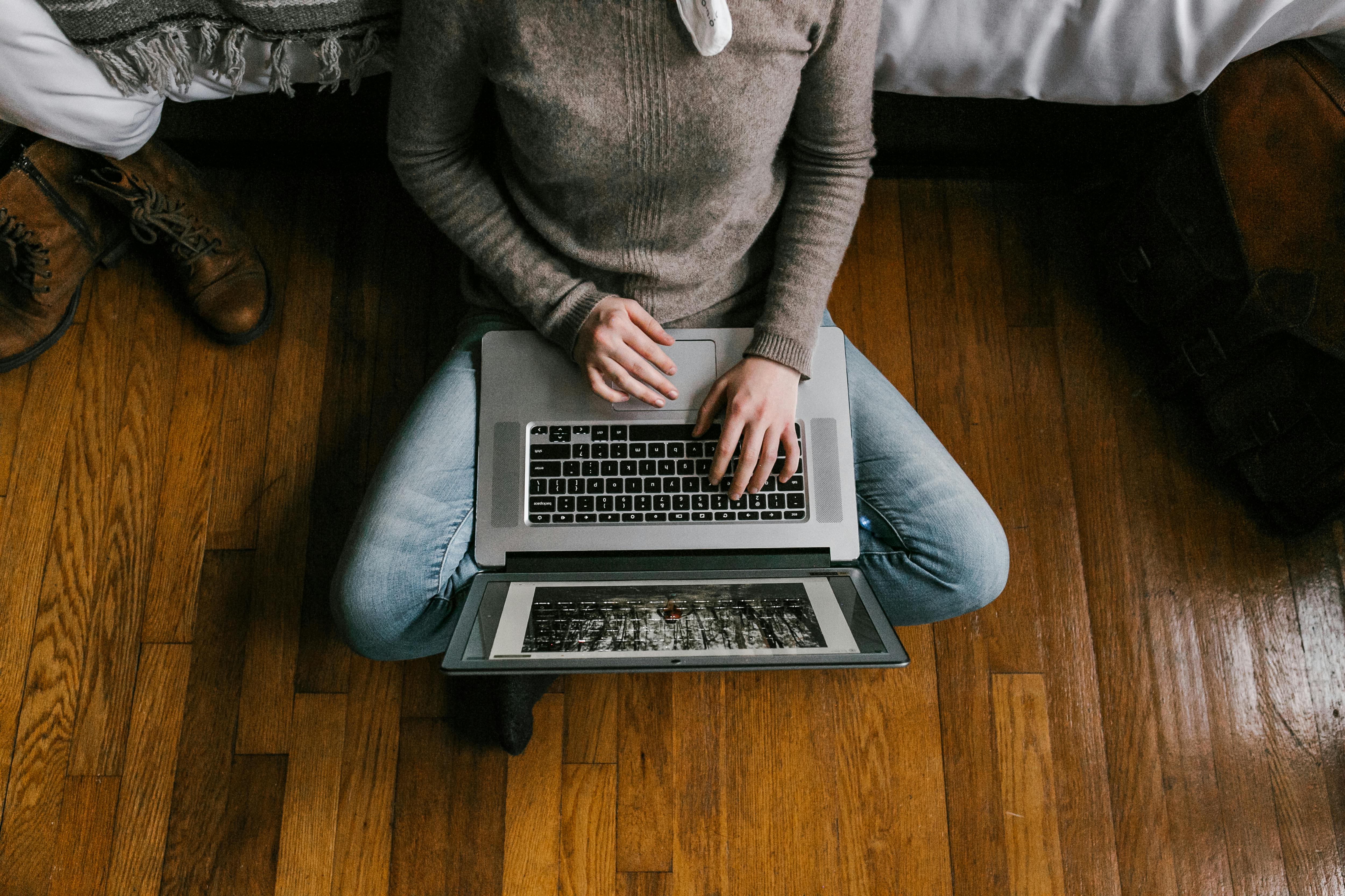 A white woman sitting criss-crossed with a laptop opened on her lap.