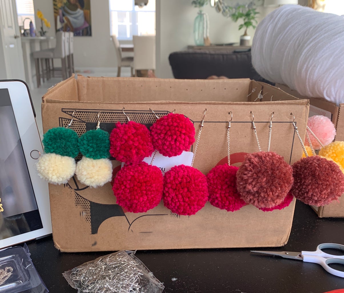 Variety of Pom-pom earrings dangling from a cardboard box